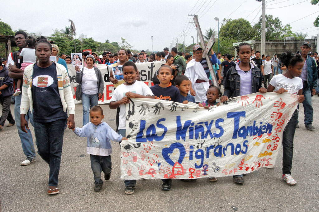 Niñas y niños sostienen una manta que expresa su presencia en la caravana de personas migrantes.