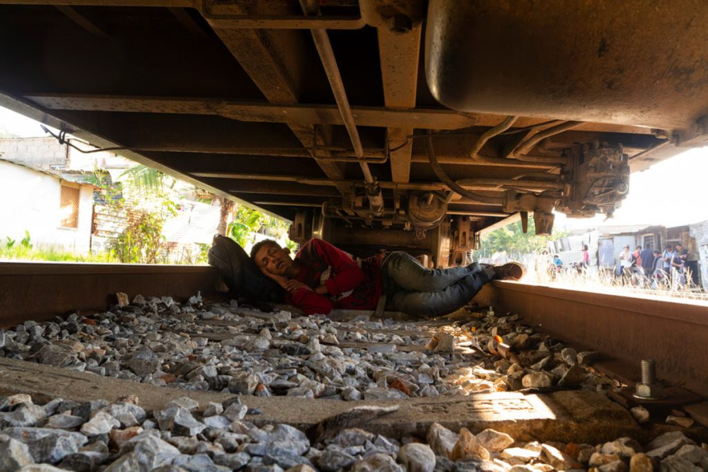 Persona migrante descansando bajo las vías del tren.