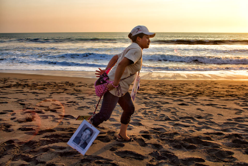 Madre lleva el retrato de su hijo mientras lo busca en la playa.