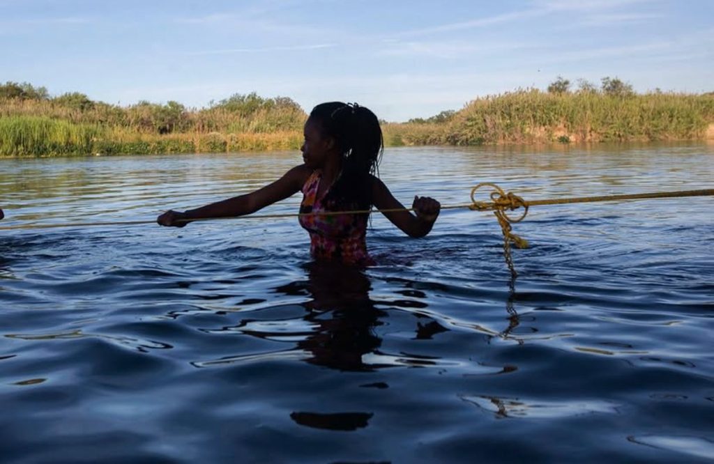 Una mujer haitiana, que se encuentra en Ciudad Acuña, Coahuila, cruza el Río Bravo sostenida de una cuerda.