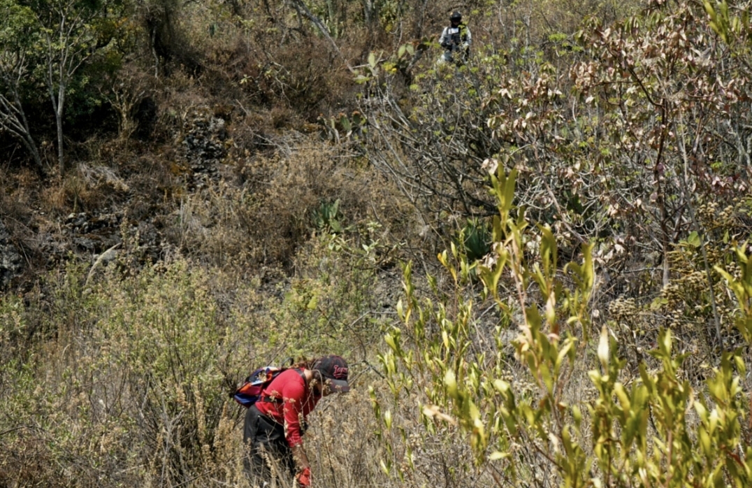 Persona solidaria buscando entre la tierra con sus manos, mientras integrante de la Guardia Nacional observa.