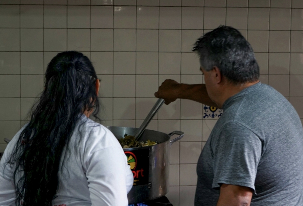 Padre y madre buscadoras calentando la comida en la cocina del Albergue Alpino Ajusco en una olla de metal.