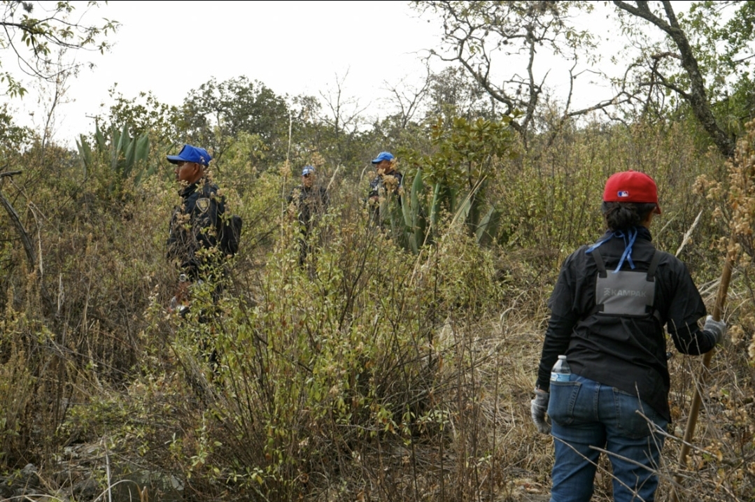 Forense solidaria revisando el terreno, mientras tres policías de proximidad de la Ciudad de México observan.